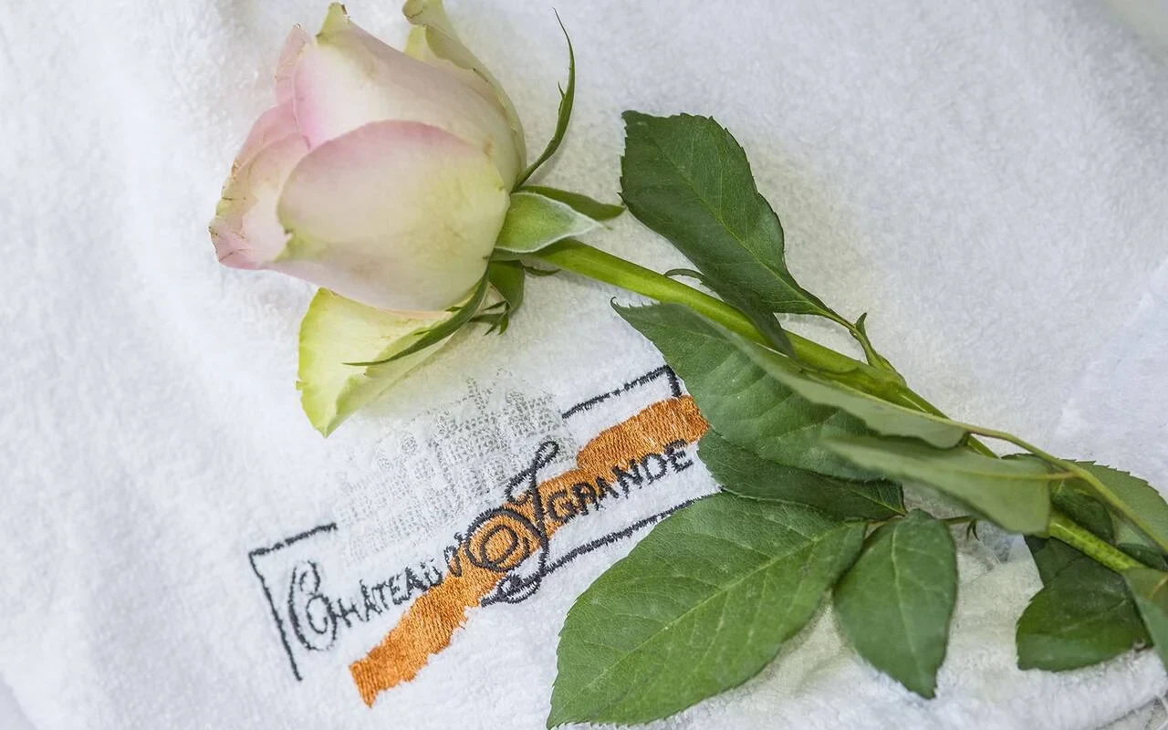 Rose pâle posée sur une serviette blanche brodée au nom du Château d’Ygrande.