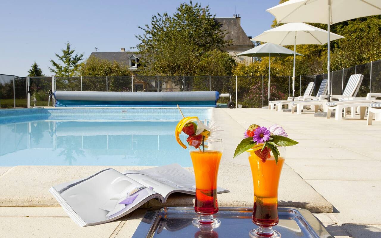 Devant la piscine extérieure du Château d’Ygrande en Auvergne, deux boissons garnies de fruits côtoient un magazine ouvert.