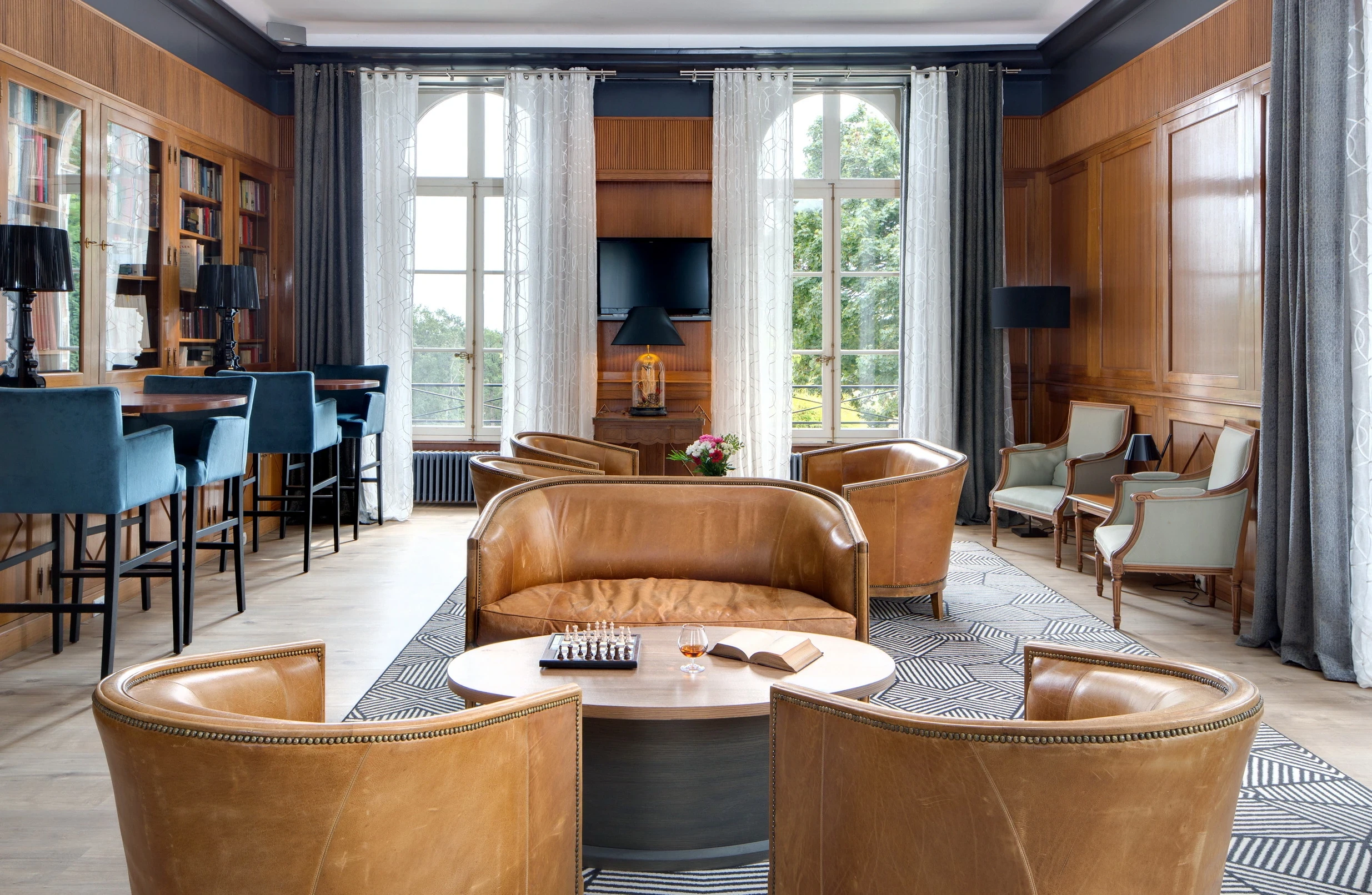 Salon d’une maison d’hôtes en Auvergne, avec canapé et fauteuils en cuir autour d’une table basse, face aux grandes fenêtres.
