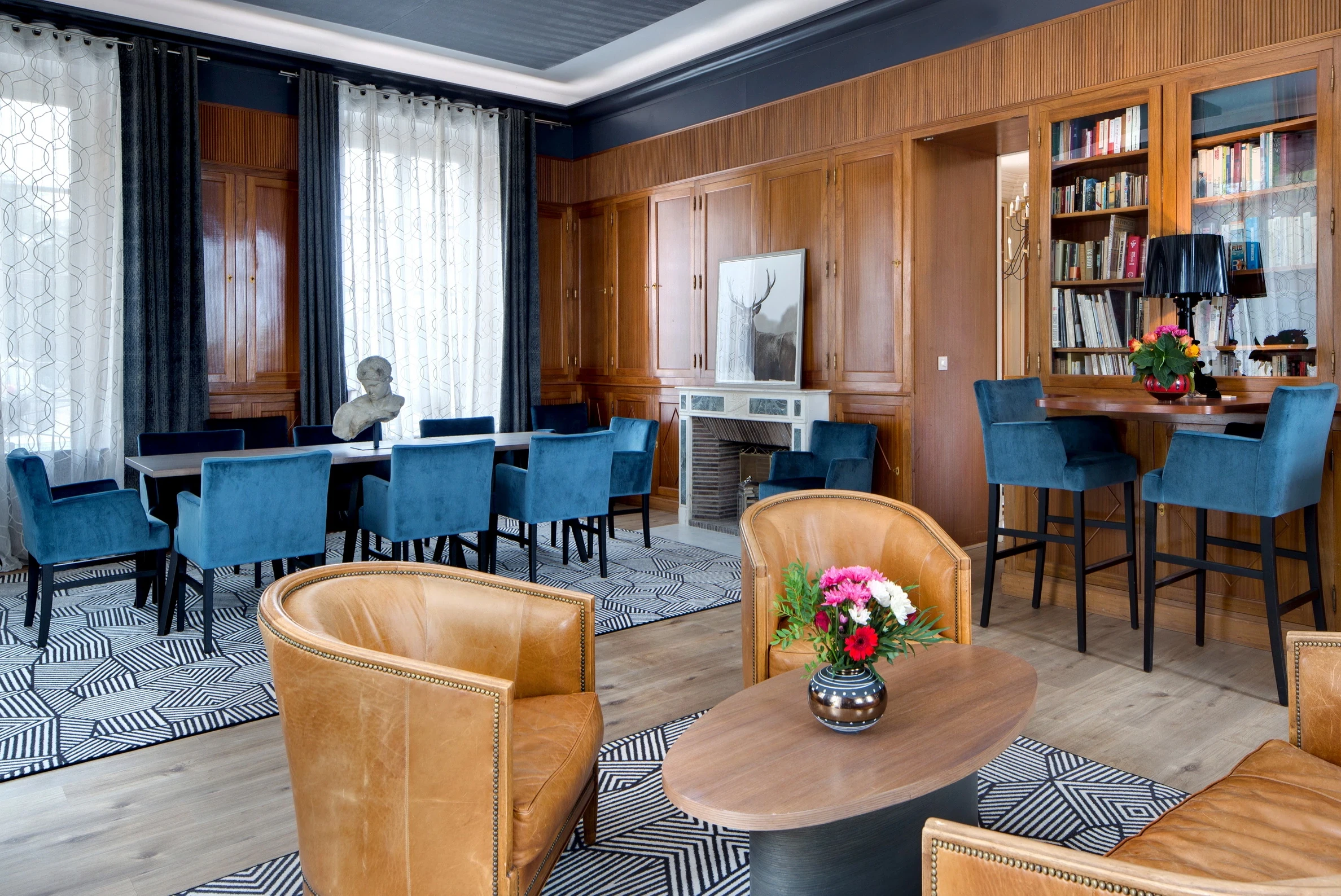 Salon-bibliothèque d’une maison d’hôtes en Auvergne, avec fauteuils en cuir et table entourée de chaises bleues.