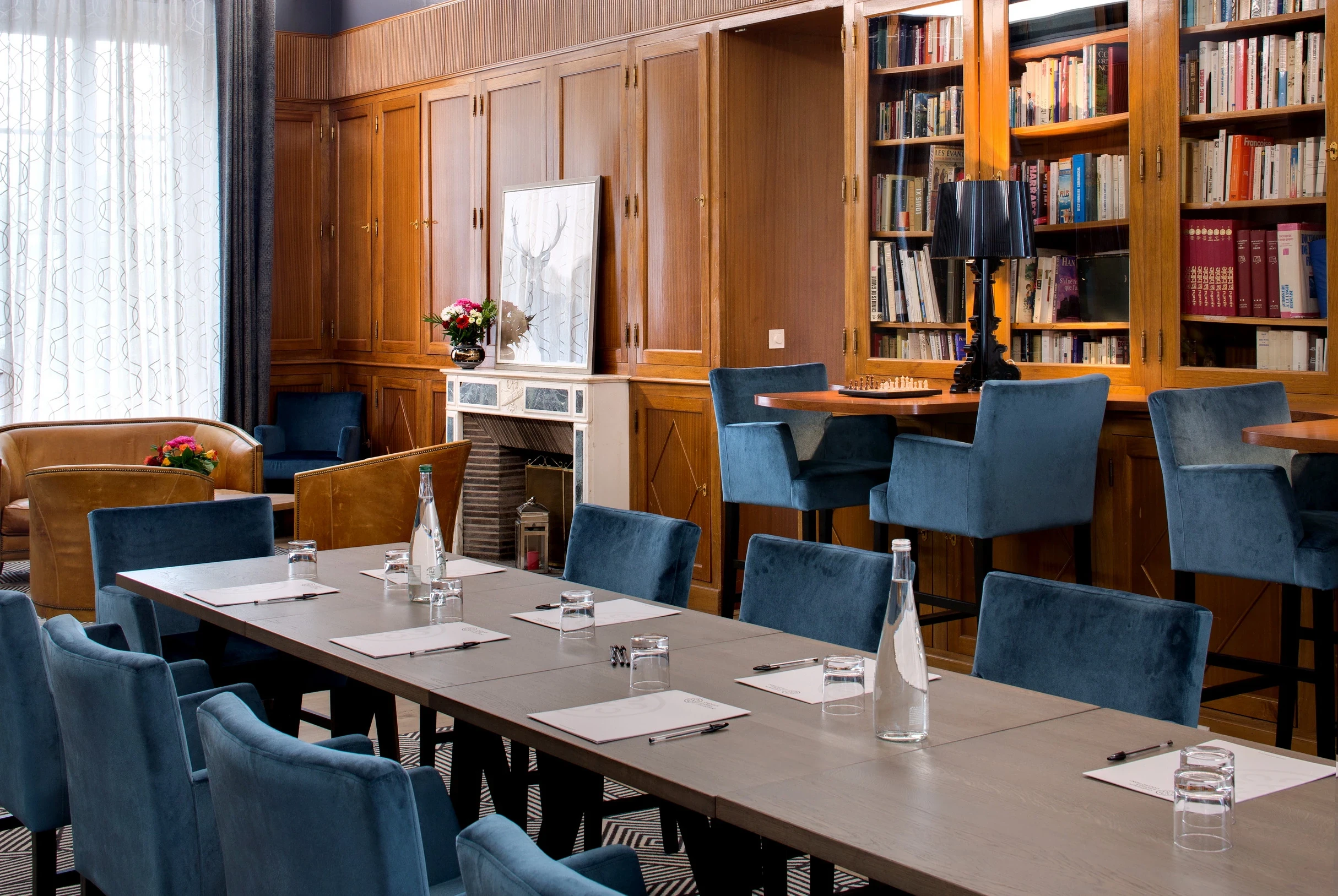 Table de réunion dans la bibliothèque du Château d’Ygrande en Auvergne, avec fauteuils bleus et cheminée.