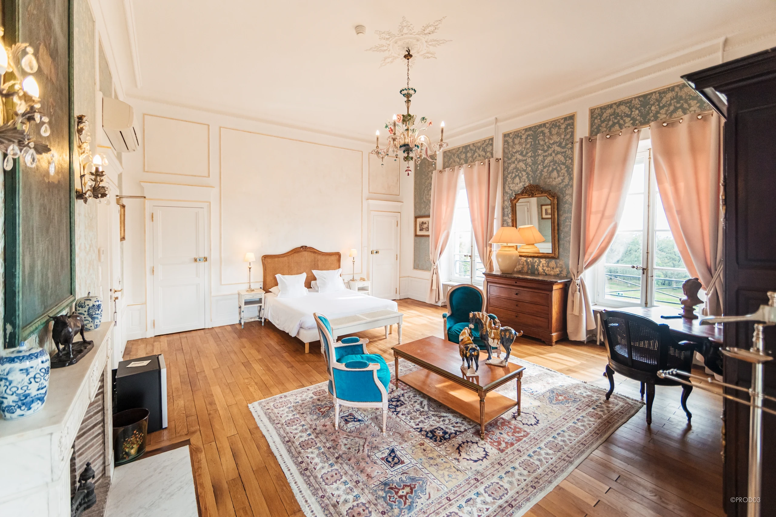 Chambre d’hôtes au Château d’Ygrande, en Auvergne, avec lit double, fauteuils turquoise et grandes fenêtres à rideaux roses.