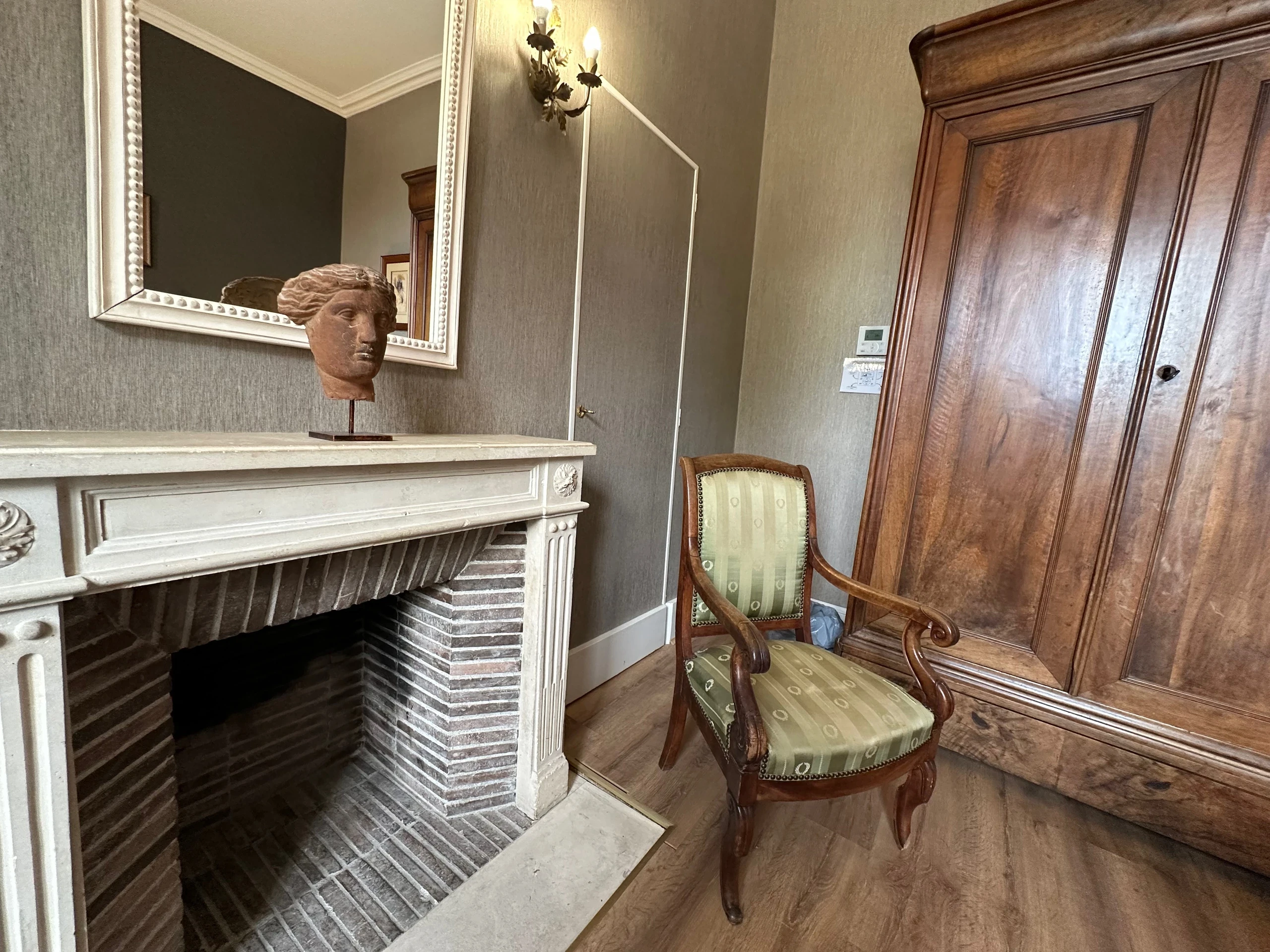 Cheminée à manteau sculpté et fauteuil vert dans une chambre d’hôtes du Château d’Ygrande en Auvergne.