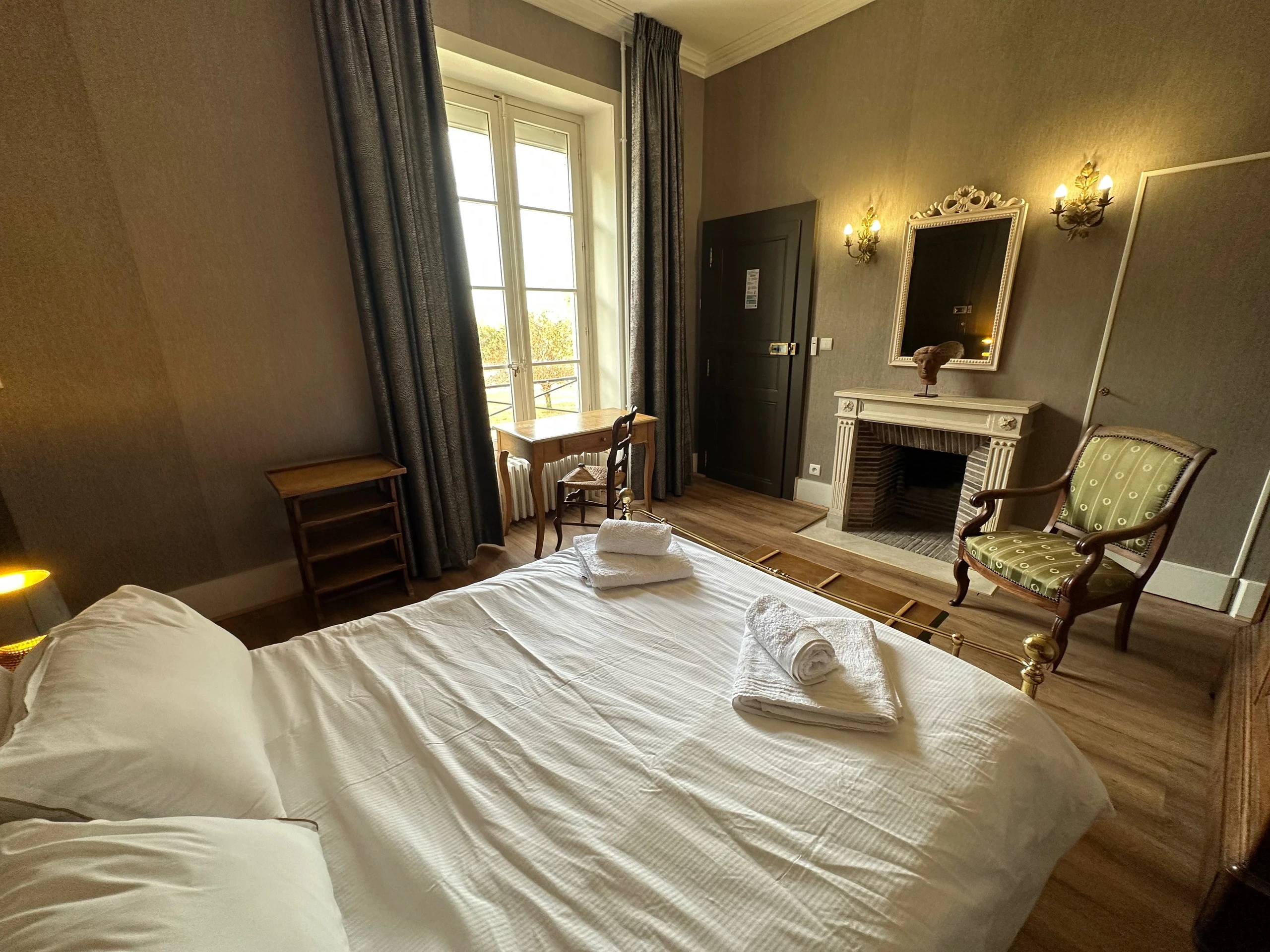 Bureau devant une grande fenêtre, lit double et cheminée dans une chambre d’hôtes en Auvergne.