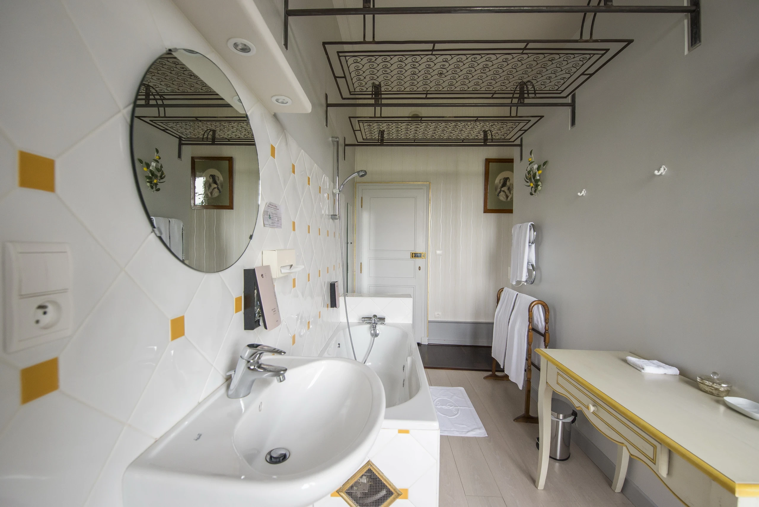 Baignoire avec douchette et lavabo sous un miroir ovale dans la salle de bains d’une chambre d’hôtes en Auvergne.