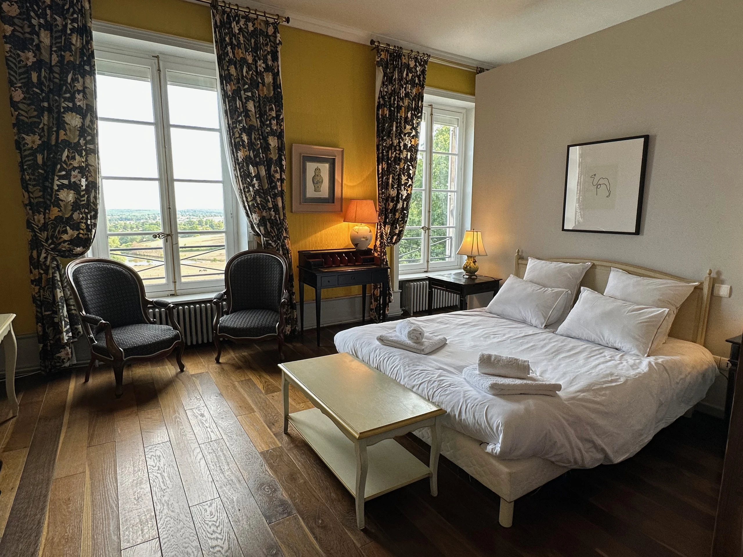 Chambre d’hôtes au Château d’Ygrande en Auvergne, avec lit double, deux fauteuils et grandes fenêtres sur la campagne.
