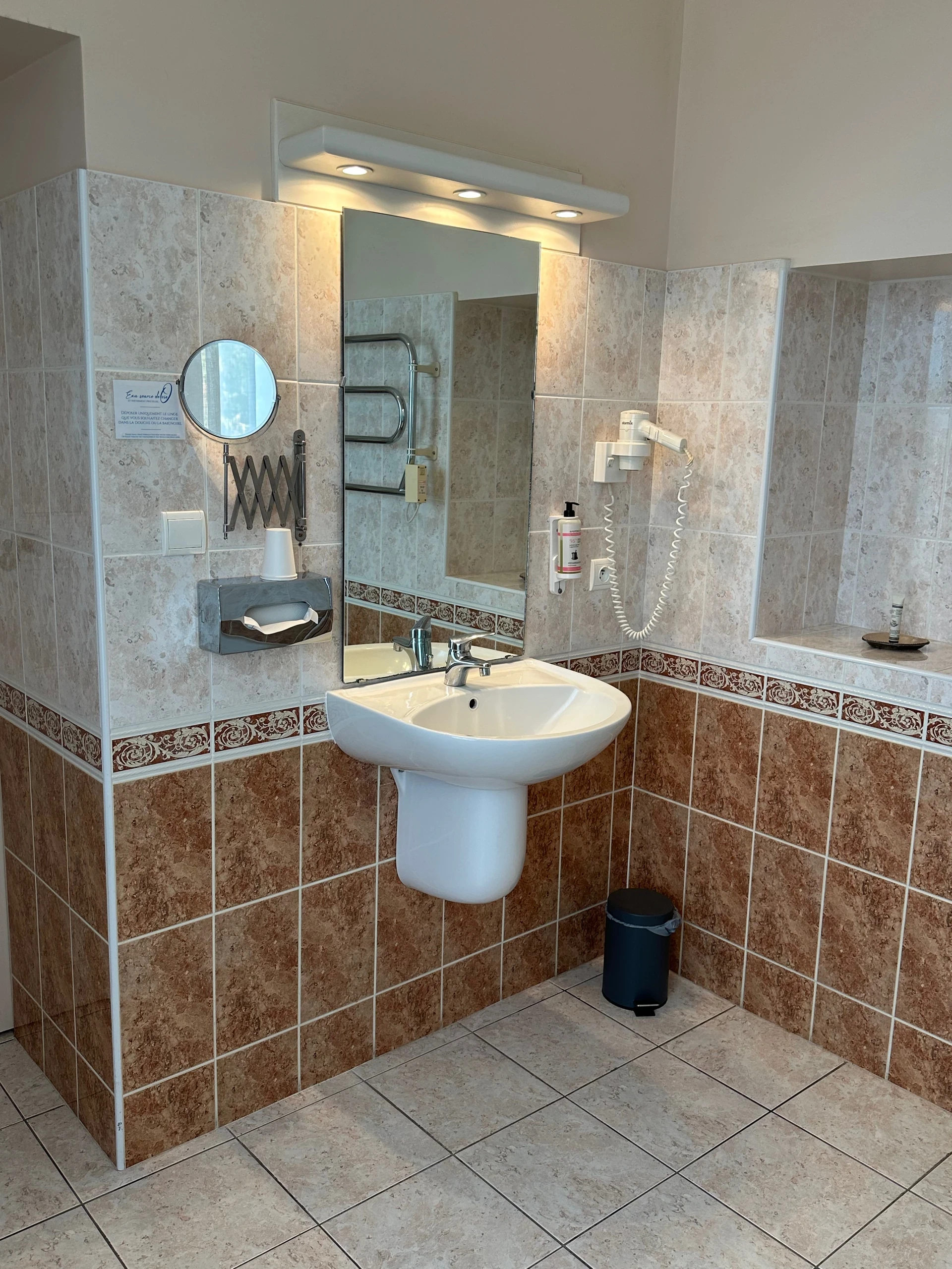 Salle de bain d’une chambre d’hôtes en Auvergne, avec lavabo, grand miroir éclairé et sèche-cheveux mural.