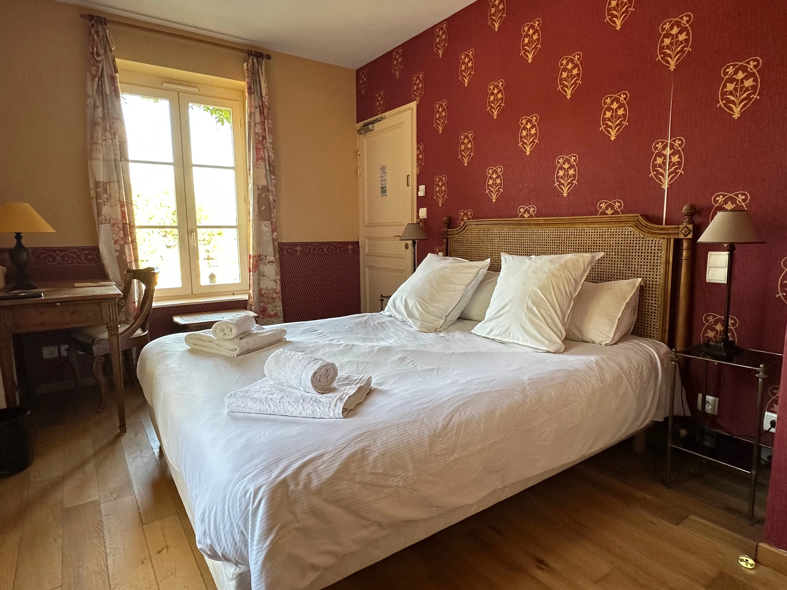 Chambre d’hôtes du Château d’Ygrande en Auvergne, avec lit double à tête cannée et mur rouge à motifs dorés.