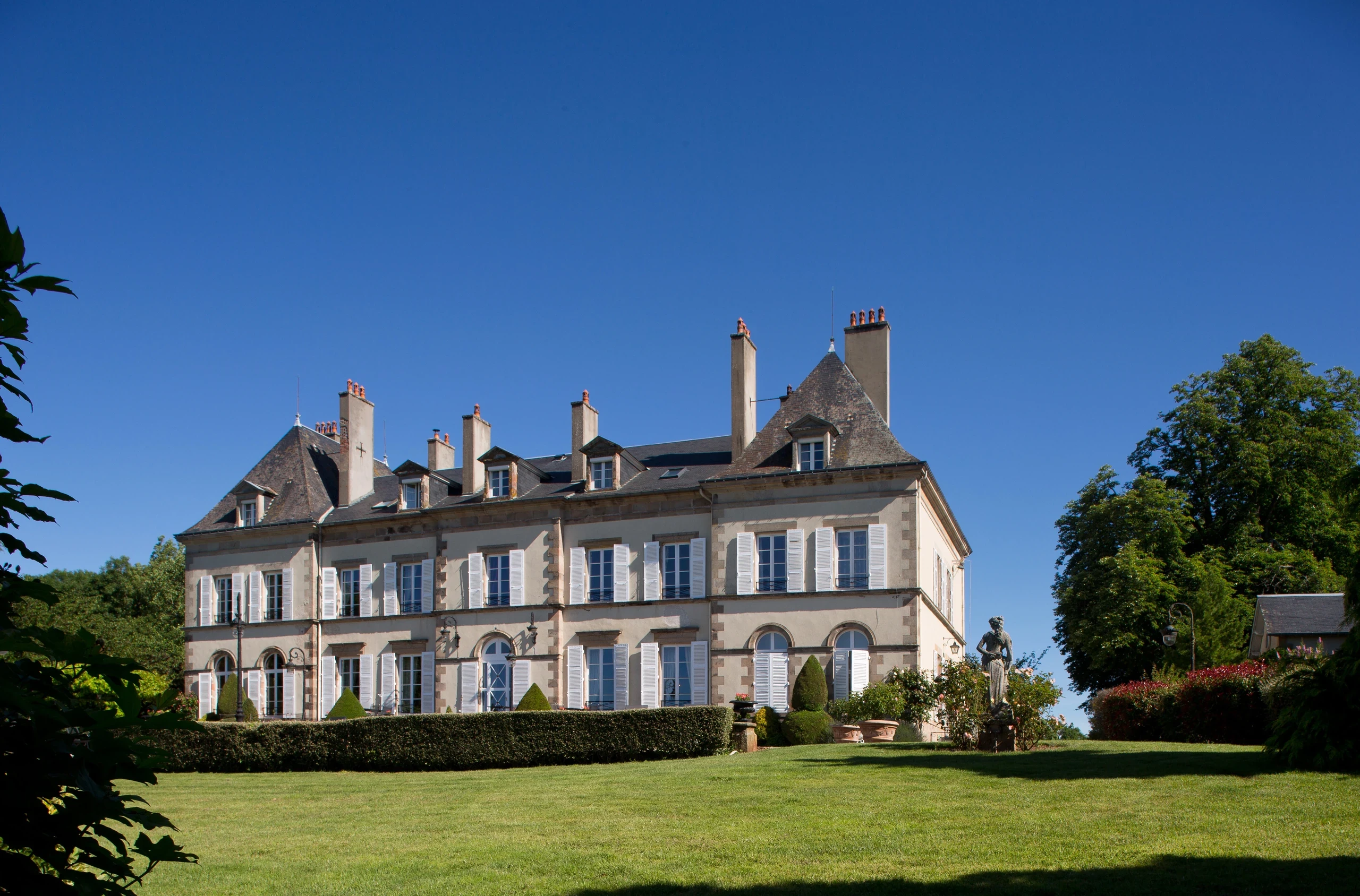 Façade du Château d’Ygrande en Auvergne vue depuis le jardin, avec pelouse et haies taillées.