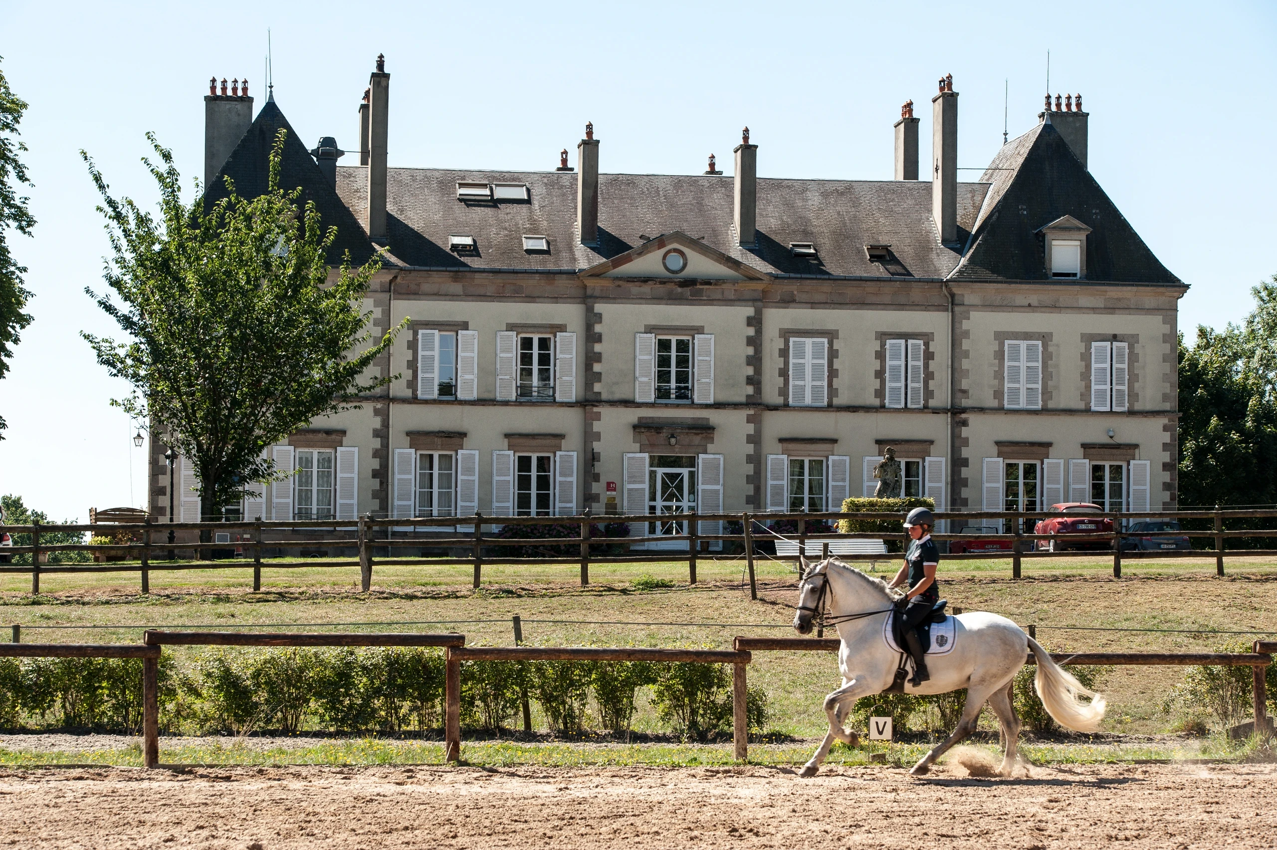 Personne montant un cheval blanc dans la carrière devant le Château d’Ygrande en Auvergne.