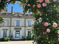 Façade du Château d’Ygrande en Auvergne, encadrée par une arche de roses roses.