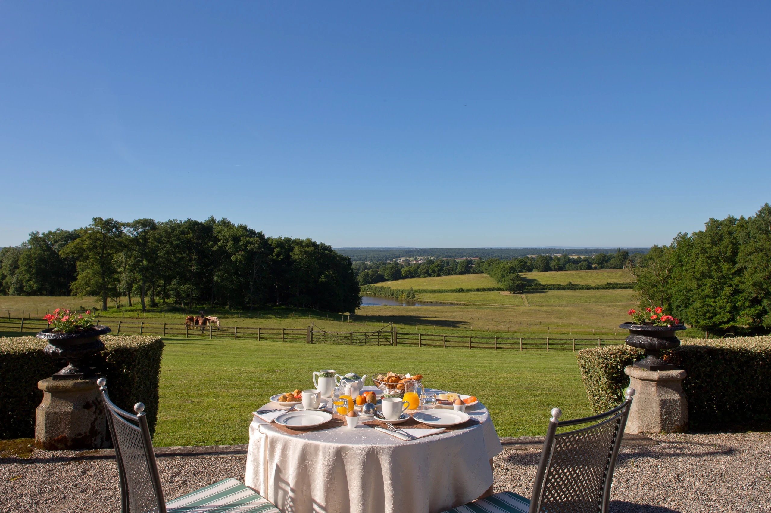 Petit-déjeuner en terrasse au Château d’Ygrande en Auvergne, face aux prairies où paissent des chevaux.