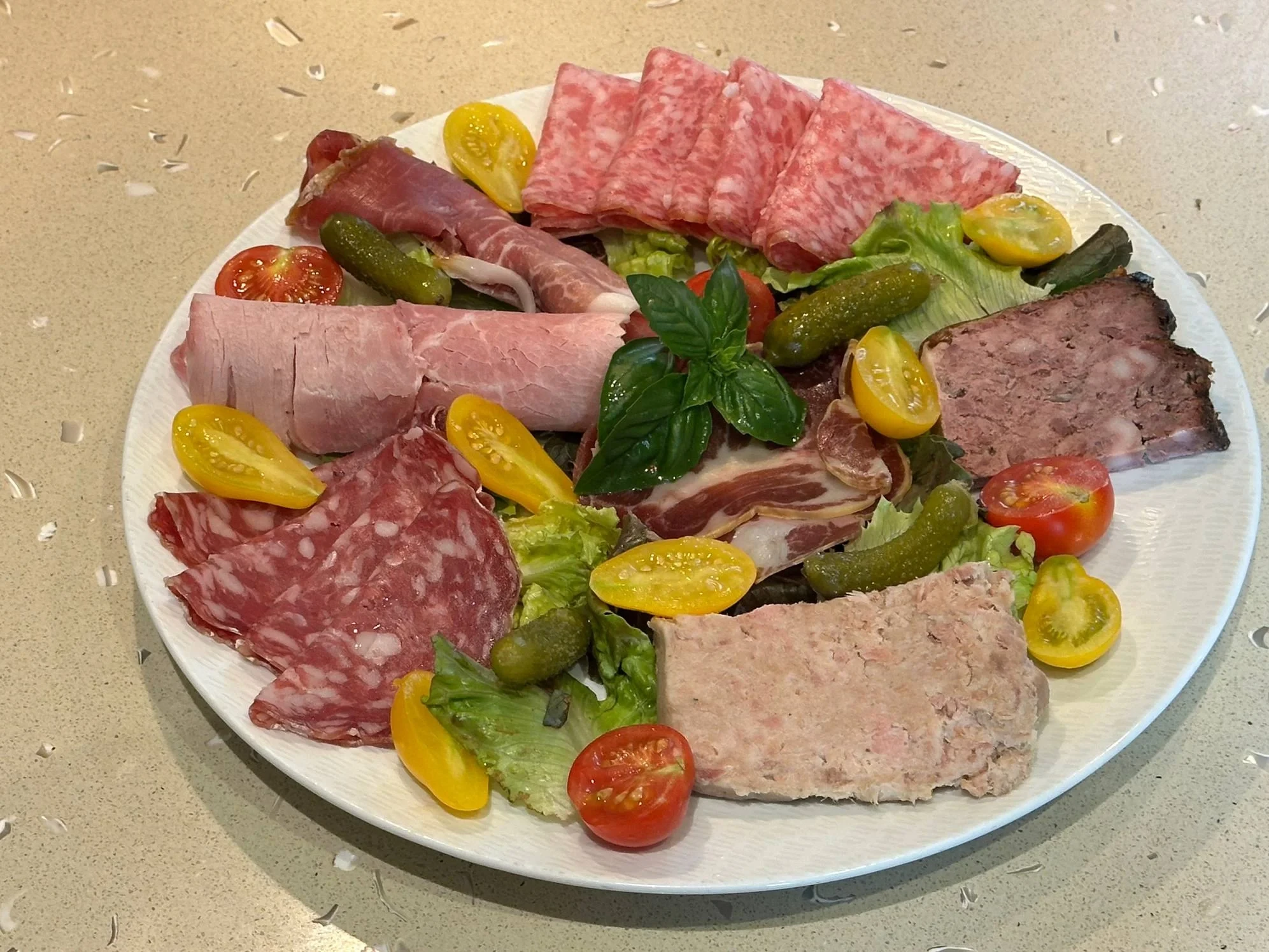 Assiette de charcuterie et de pâtés, avec cornichons, salade et tomates cerises.