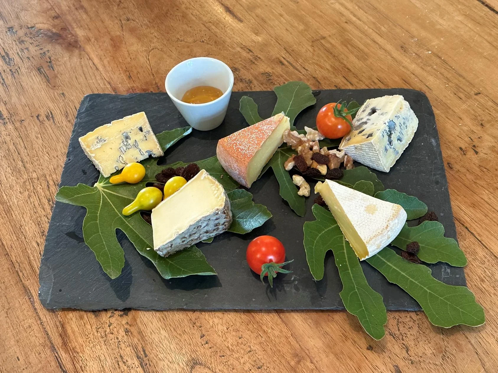 Assortiment de cinq fromages sur ardoise, avec noix et raisins secs.