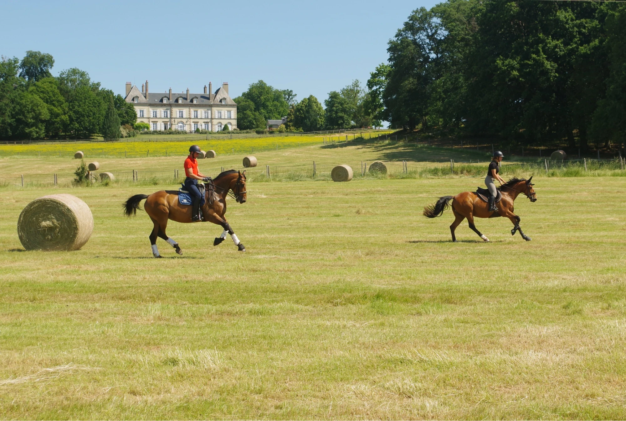 Deux cavaliers traversent une prairie en Auvergne, avec un château à l’arrière-plan.