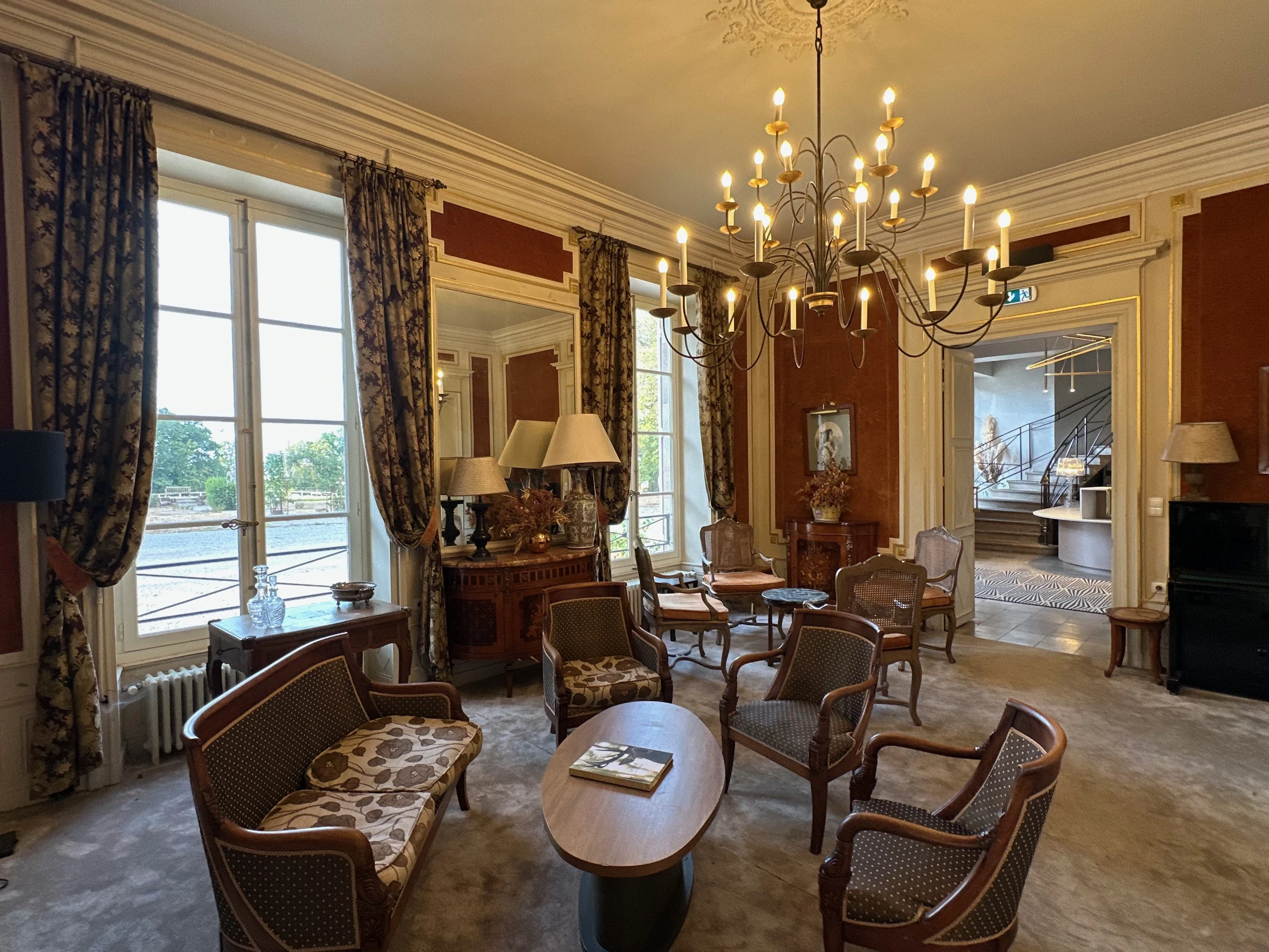 Canapé et fauteuils autour d’une table ovale dans le salon d’une maison d’hôtes en Auvergne, éclairé par de hautes fenêtres.