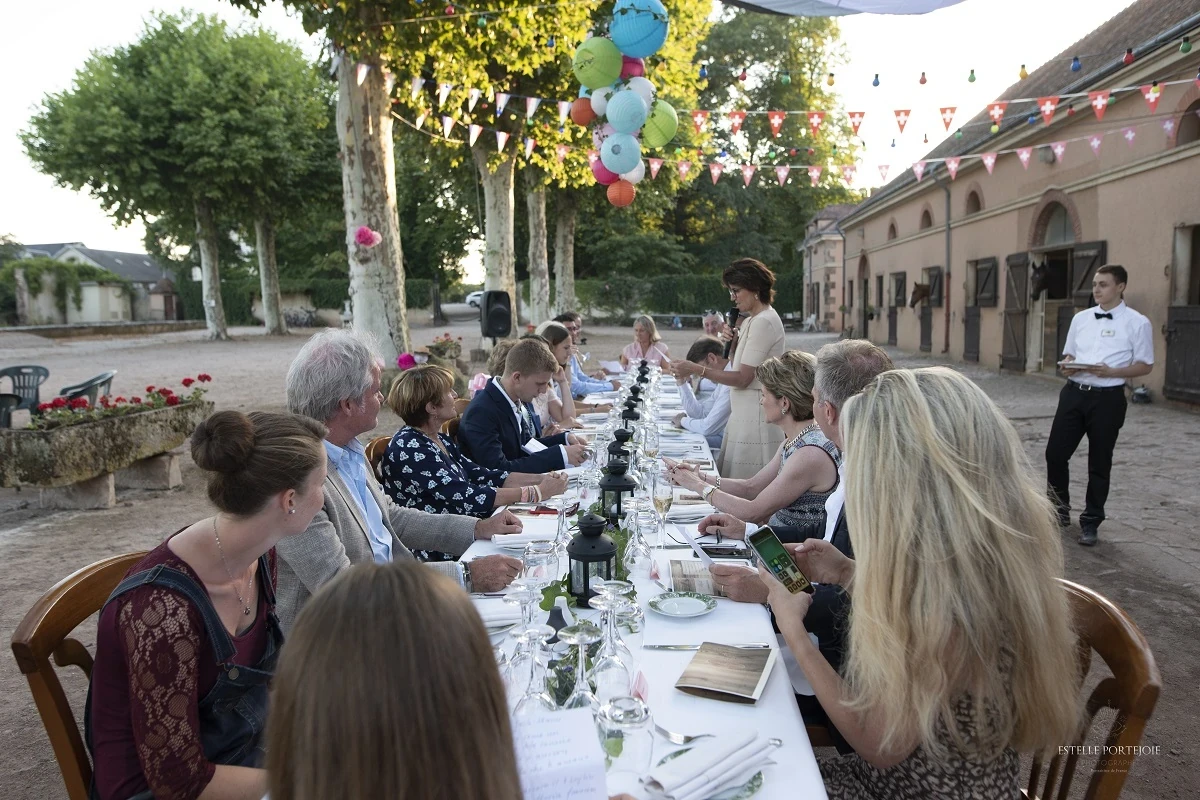 Invités attablés sous les arbres au Château d’Ygrande, en Auvergne, avec une intervenante au micro.