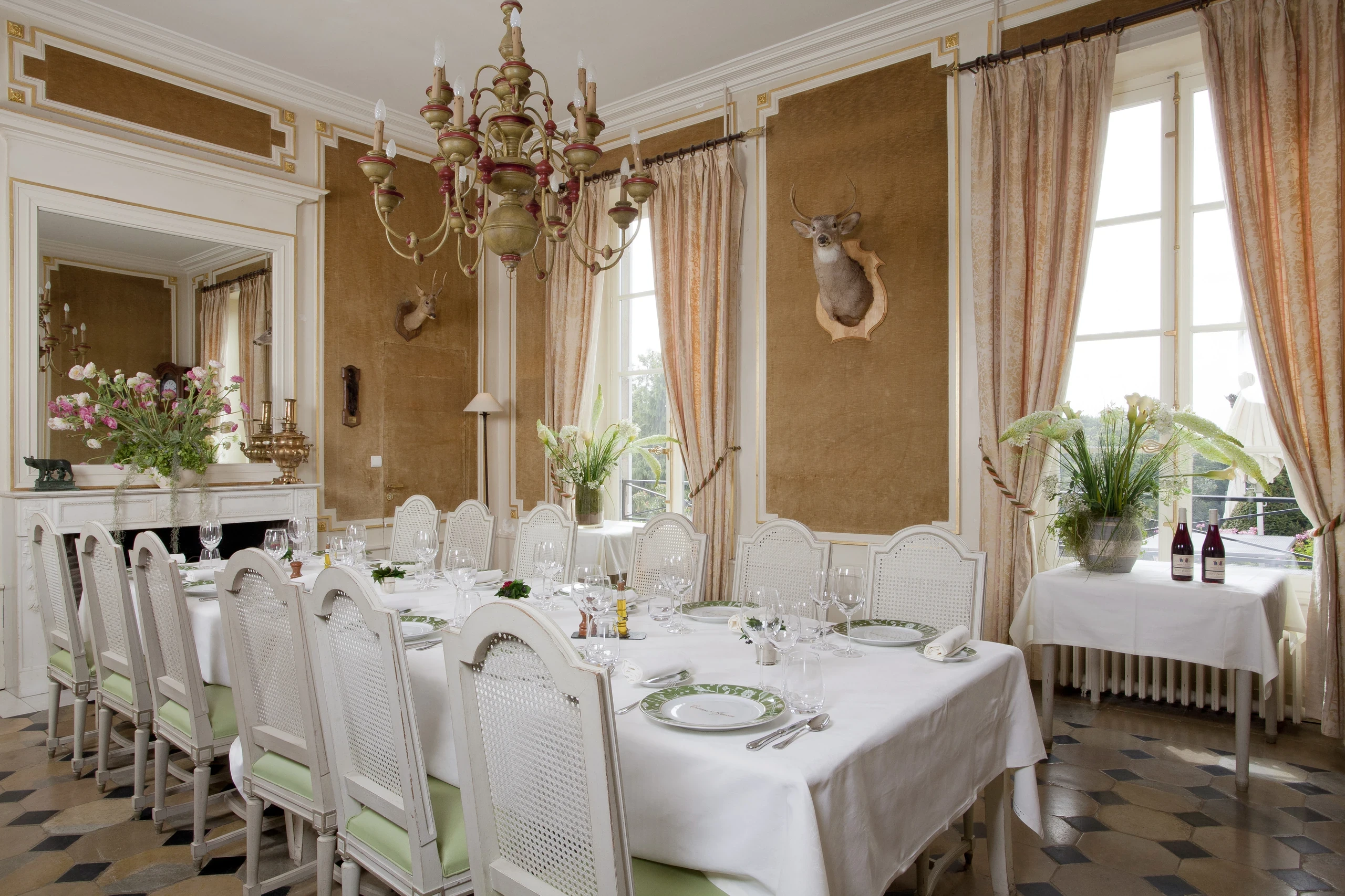 Salle à manger du Château d’Ygrande en Auvergne, avec une longue table dressée près de hautes fenêtres et un sol à motifs géométriques.